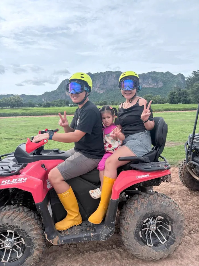ครอบครัวพ่อแม่ลูกนั่งรถ ATV คันเดียวกัน สวมหมวกกันน็อคชูสองนิ้วให้กล้อง
