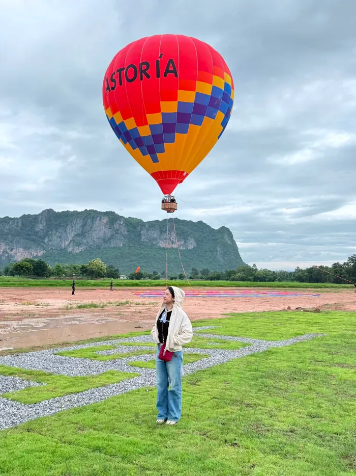 คู่รักยืนถ่ายรูปบนลานหญ้าโดยมีบอลลูน ASTORIA ลอยอยู่เบื้องหลัง